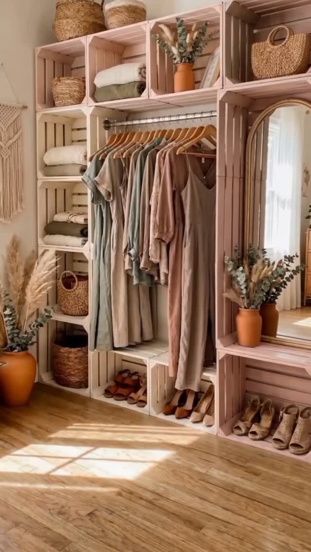 Pink wooden crate shelving unit holding folded clothes, baskets, and hanging garments in a bright room.