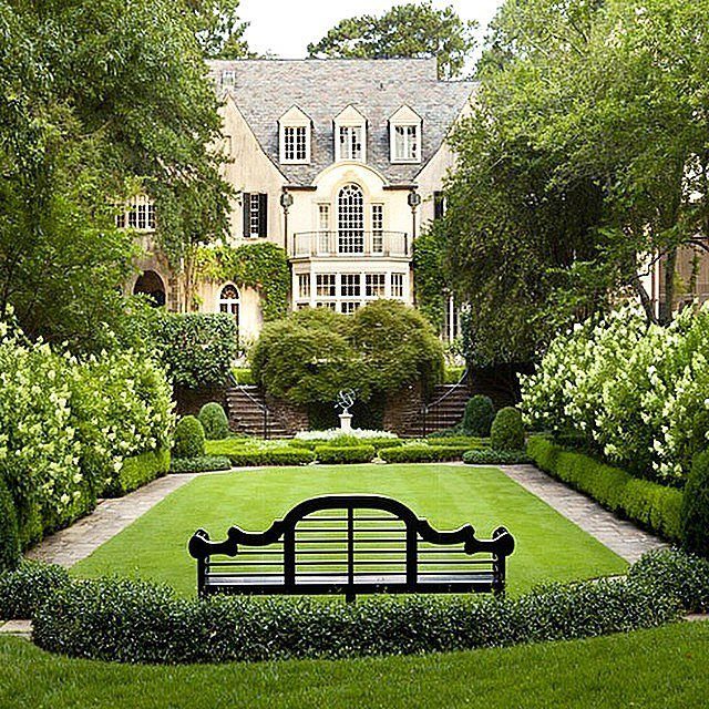 13 Estate Garden Design Ideas With Photos and Planning Tips 12 A manicured estate garden with a black bench, green lawn, and a large stone mansion in the background.
