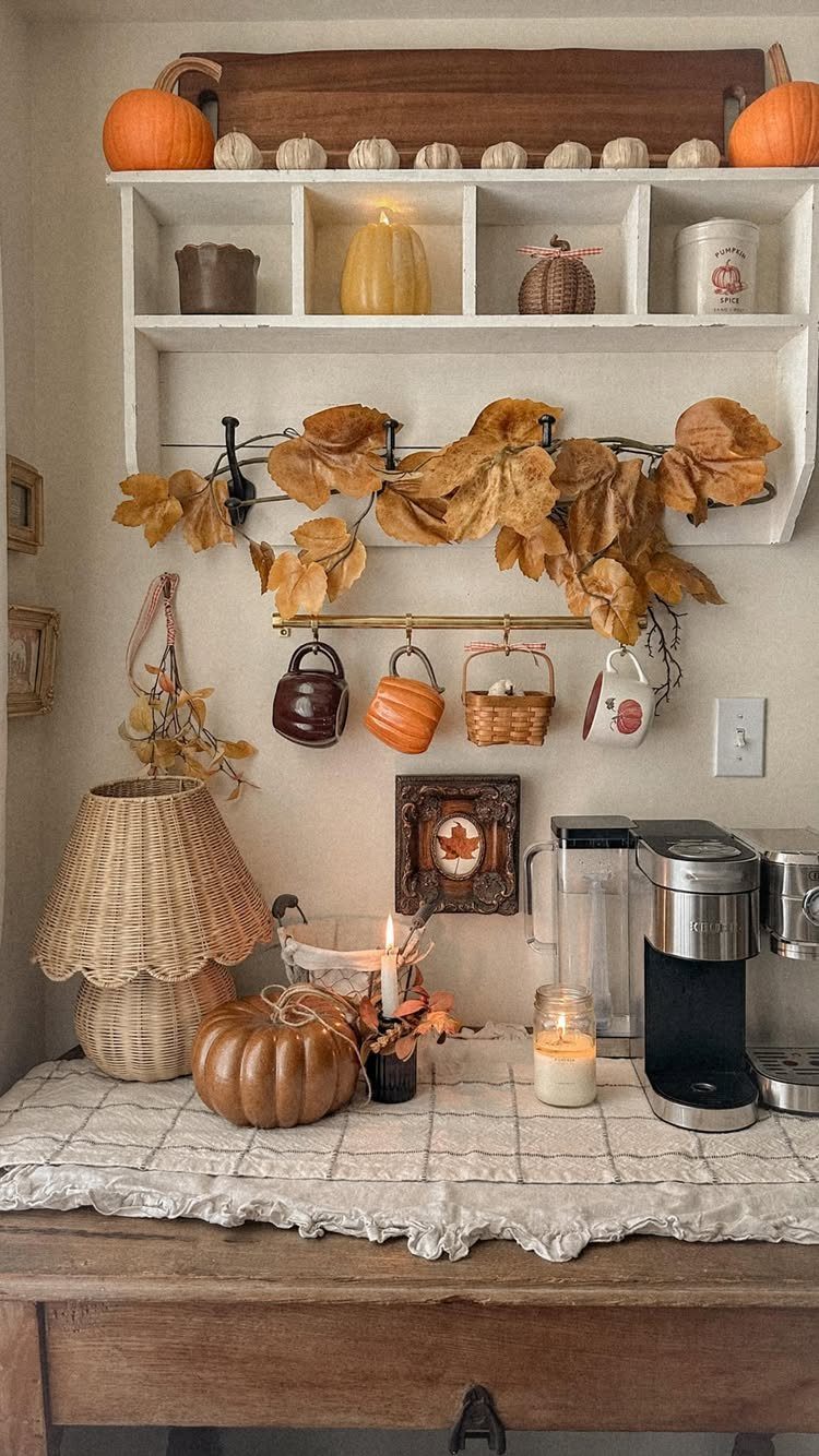 16 Farmhouse Coffee Bar Ideas for Pantry Nooks to Pallet Walls 3 Autumnal coffee bar setup with pumpkins, dried leaves, and hanging mugs on white shelves.