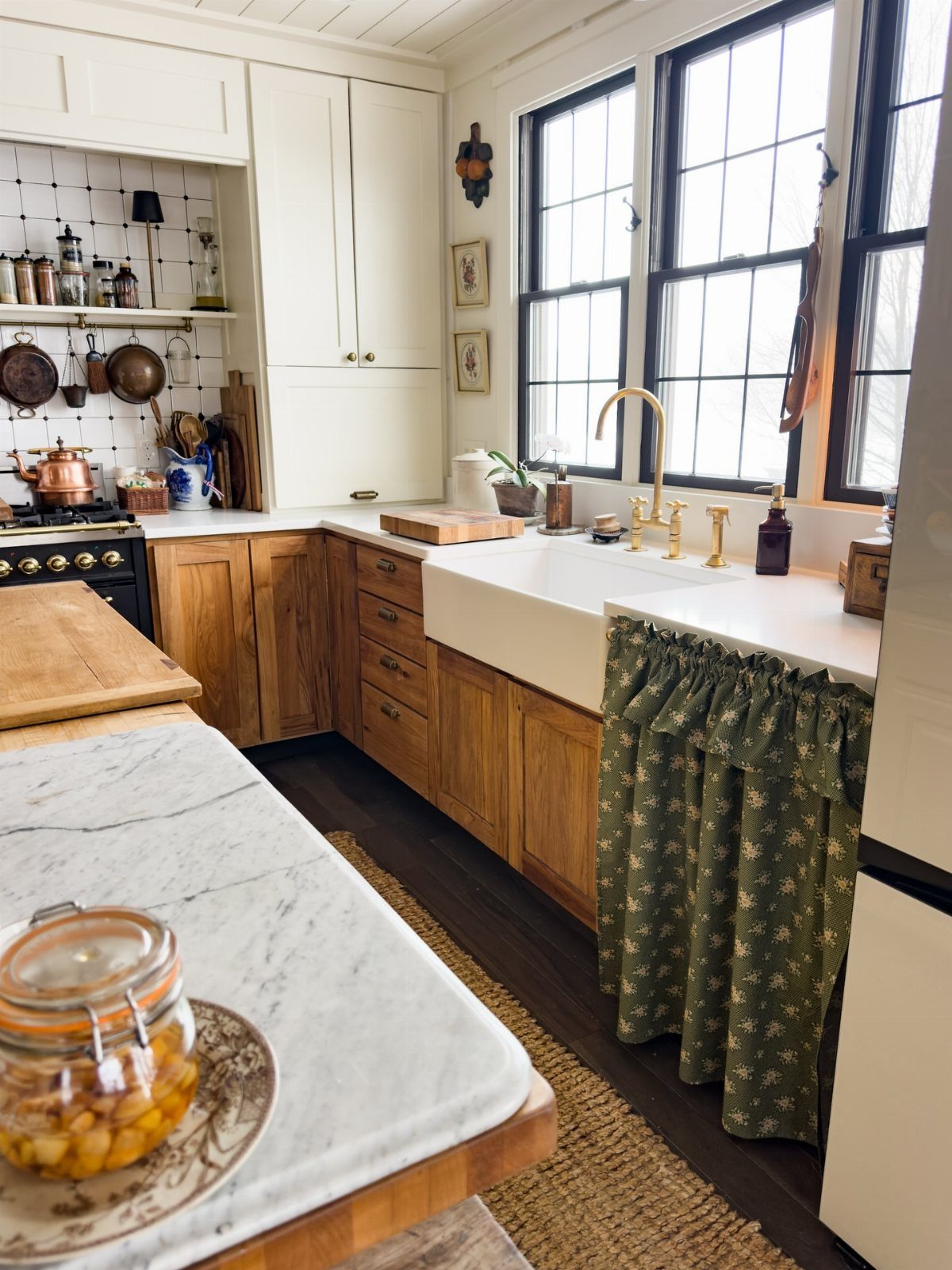A white farmhouse sink with a green patterned fabric cabinet skirt in a rustic kitchen.