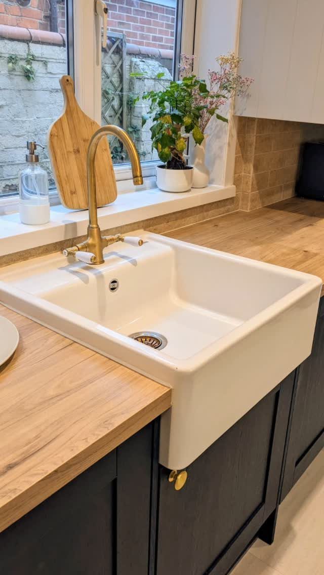 White ceramic farmhouse sink with a gold faucet set into a wooden kitchen countertop.