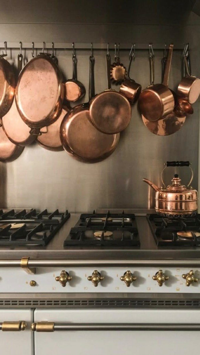 Copper pots and pans hanging from a metal rack above a stainless steel kitchen stove.