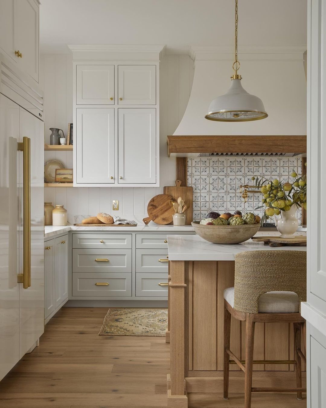A bright kitchen with white cabinets, wooden island, stone countertops, and light wood flooring.