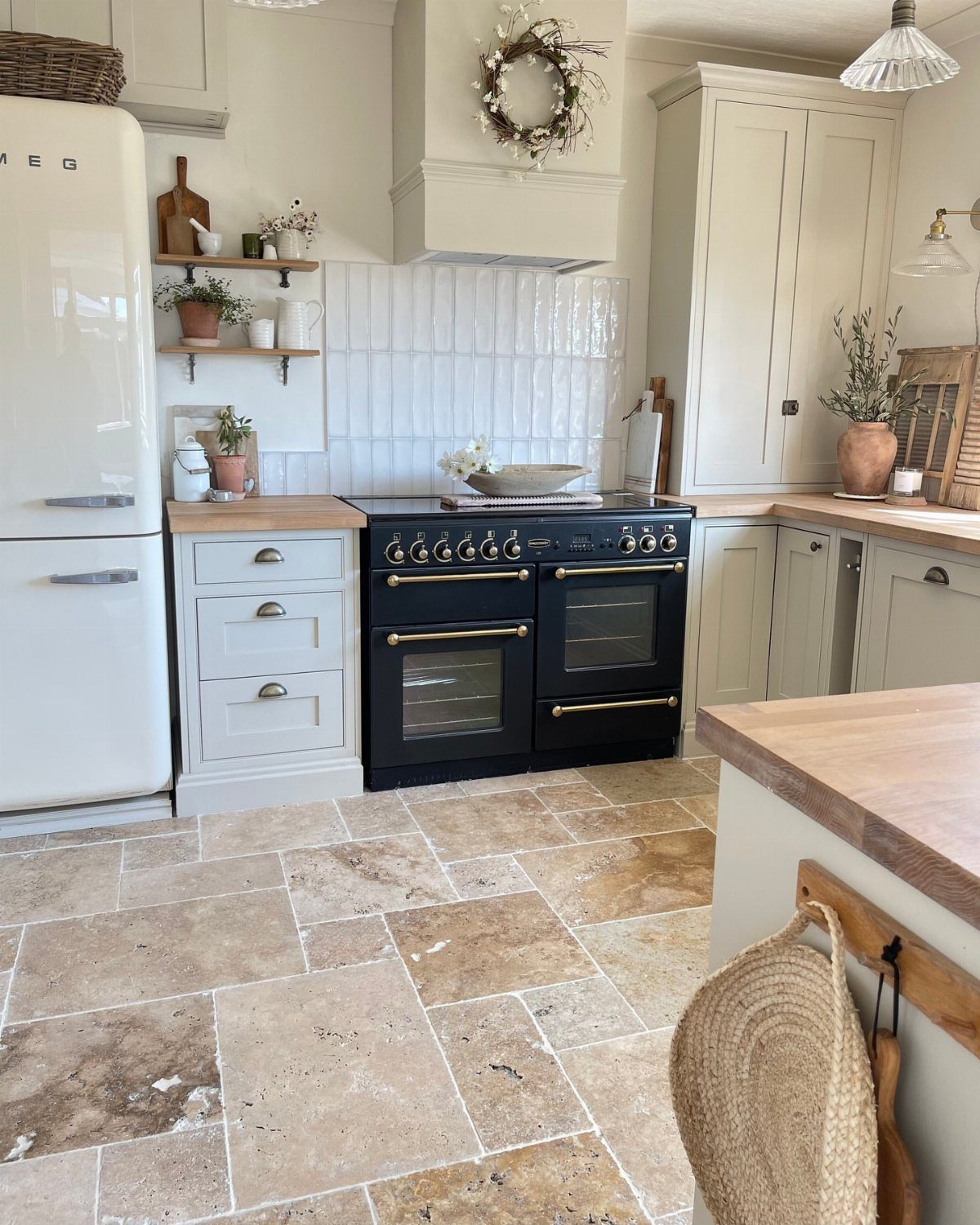 Natural stone floor tiles in a bright kitchen with cream cabinets and a black stove.