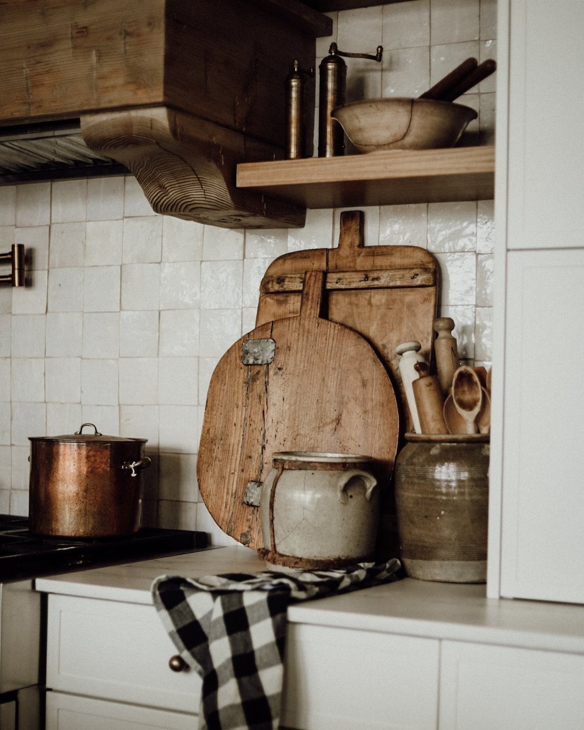 Rustic wooden cutting boards leaning against a white tiled kitchen backsplash near ceramic crocks.