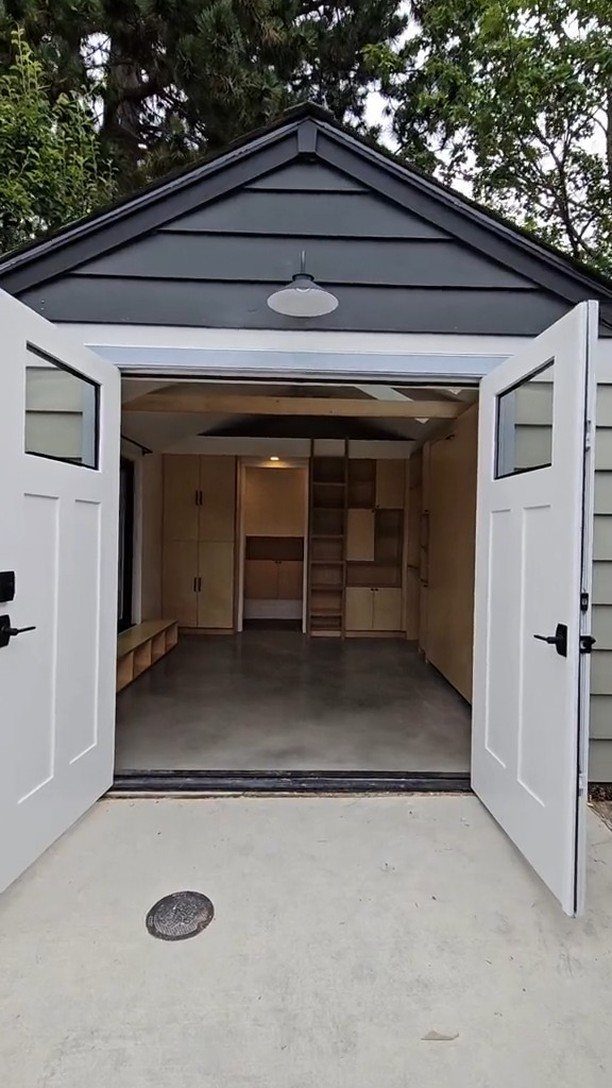 Open white garage doors revealing a modern interior with light wood cabinetry and grey concrete floors.
