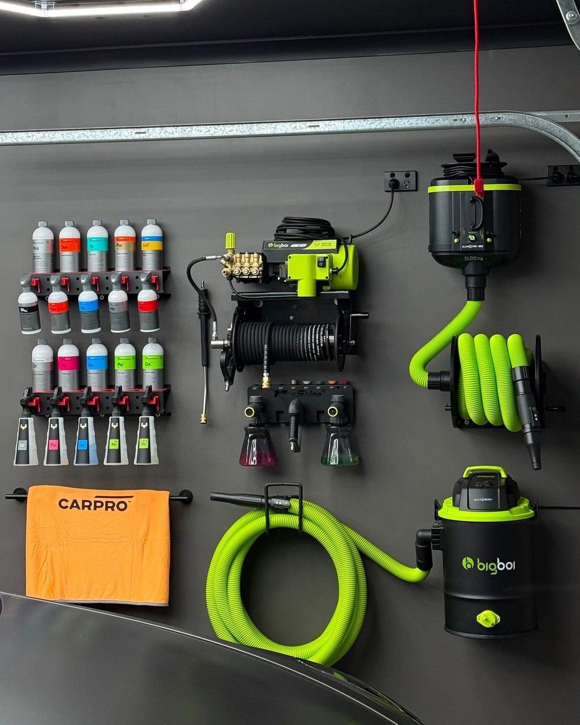 Organized cleaning equipment and colorful spray bottles mounted on a dark grey garage wall.