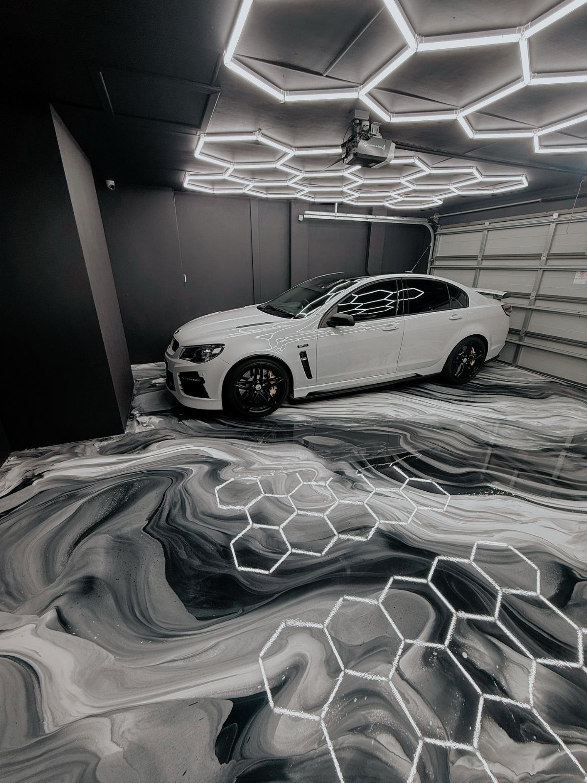 White luxury sedan parked on a swirling black and white epoxy garage floor.