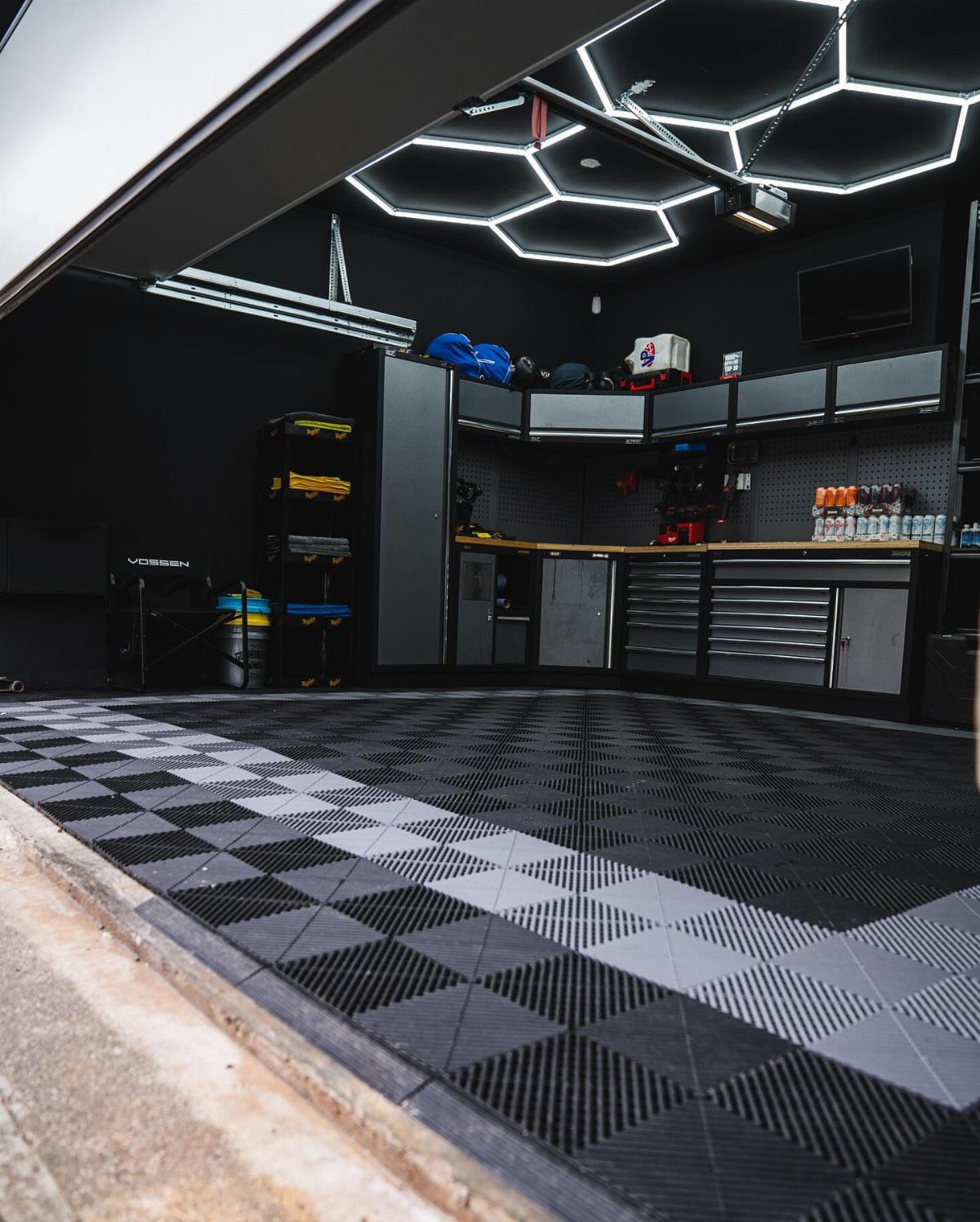 Black and grey checkered modular floor tiles in a modern, dark-themed garage interior.