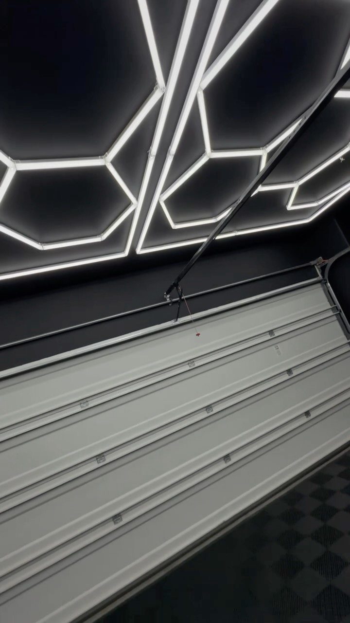 Geometric white LED light strips forming hexagonal patterns on a dark garage ceiling.