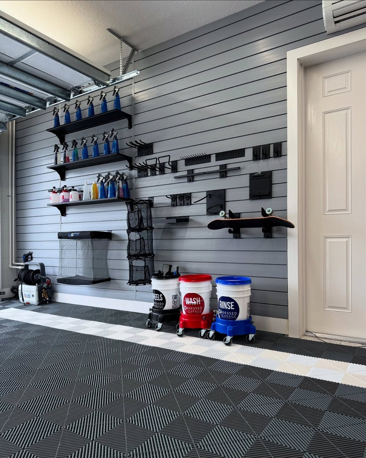 Grey slatwall system with black shelves and hooks installed in a modern garage setting.