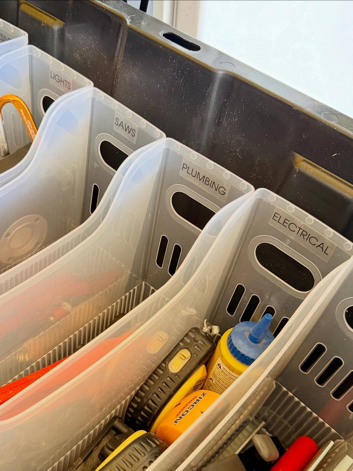 Clear plastic storage bins labeled for different tasks containing various tools and supplies.