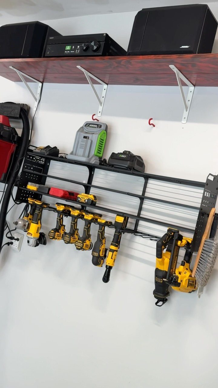 Black metal wall rack holding various yellow power tools against a white wall.