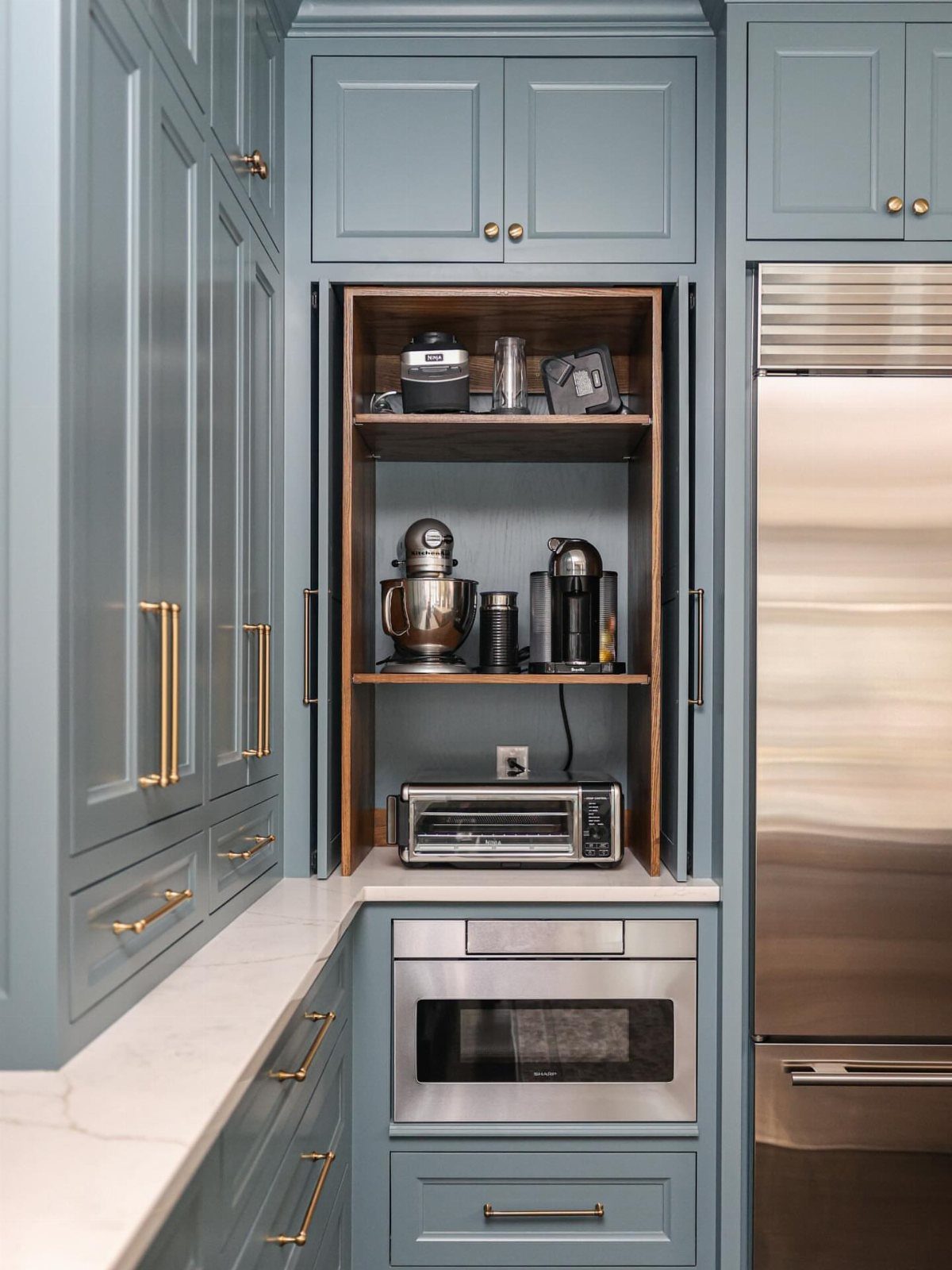 Blue-grey kitchen cabinetry with white marble countertops and stainless steel appliances.