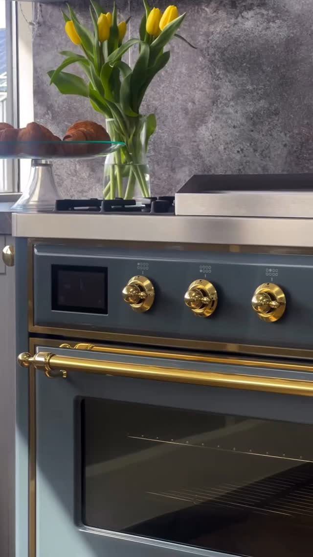 Grey blue kitchen stove with gold knobs and handles next to yellow tulips and croissants.