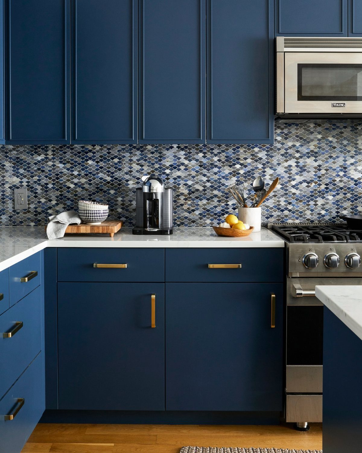 Blue kitchen cabinets with gold hardware and a blue and grey mosaic tile backsplash.