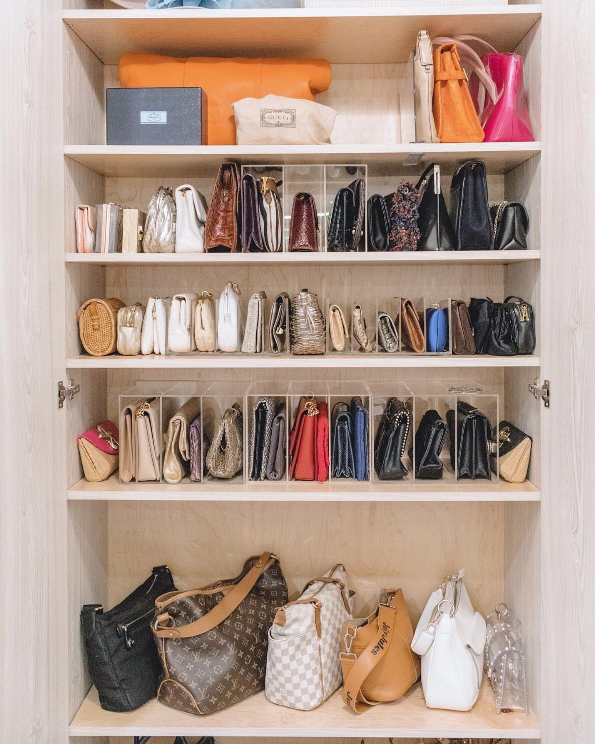 Various handbags organized on wooden closet shelves using clear acrylic dividers.
