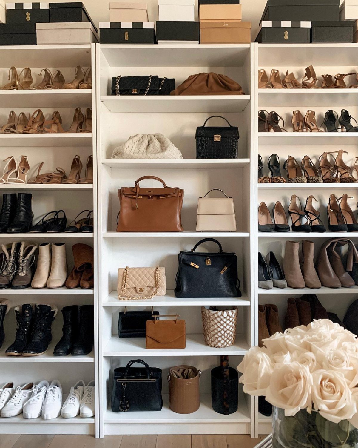 White bookcase shelves organized with various designer handbags and rows of stylish shoes.