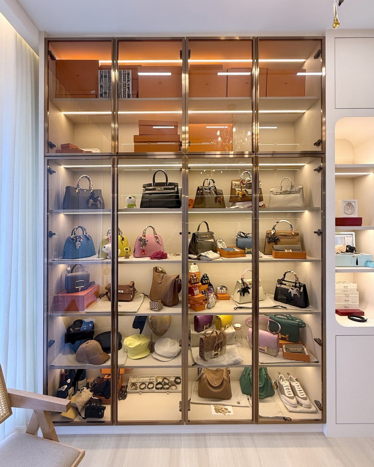 A large white built-in cabinet with glass doors displaying a collection of handbags and luxury boxes.