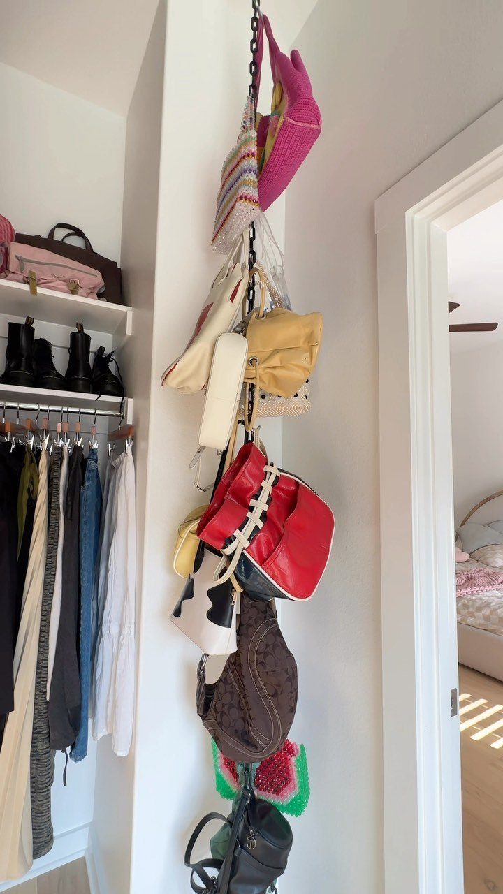 Multiple colorful handbags hanging vertically from a black chain organizer in a white room.