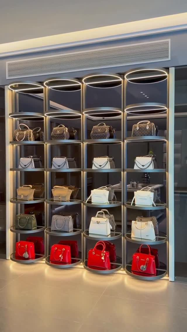 Four tall rotating shelving units displaying various colorful designer handbags under bright LED lights.