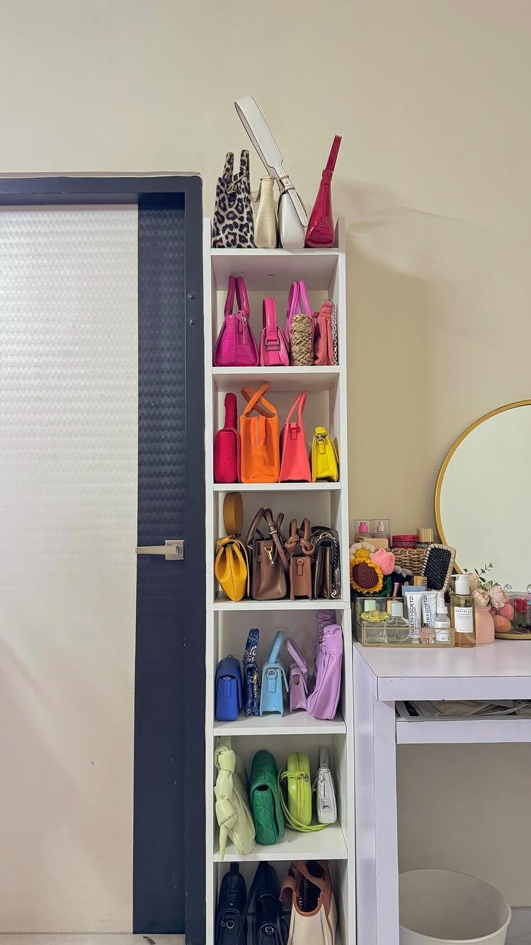 A white shelving unit displaying many colorful handbags organized by their color spectrum.
