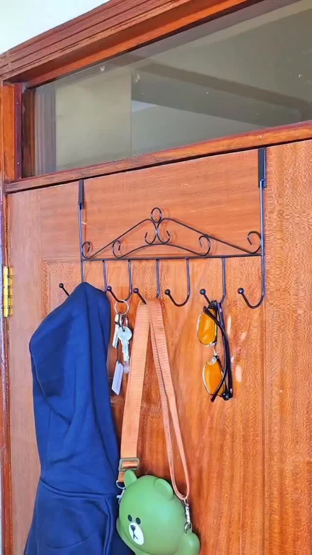 Black metal decorative wall rack with hooks hanging items on a wooden door.