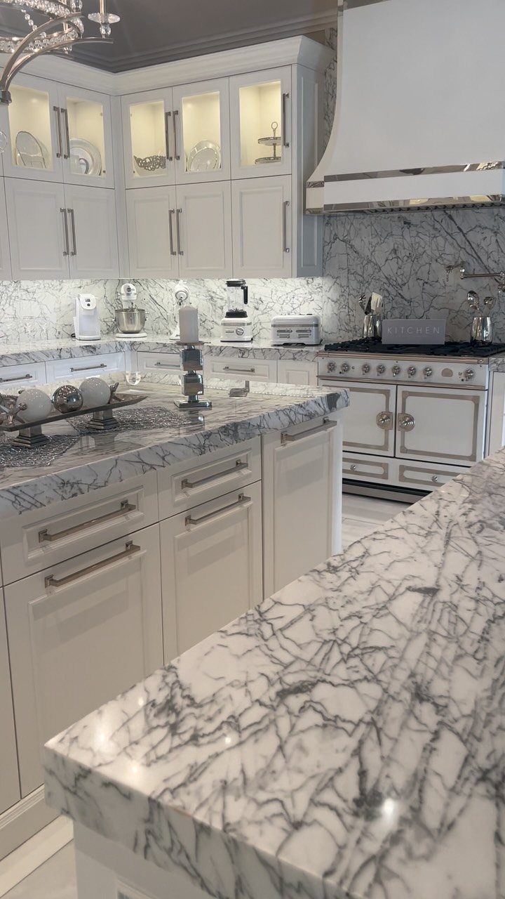 White kitchen cabinets and marble countertops with grey veining in a bright, luxurious setting.