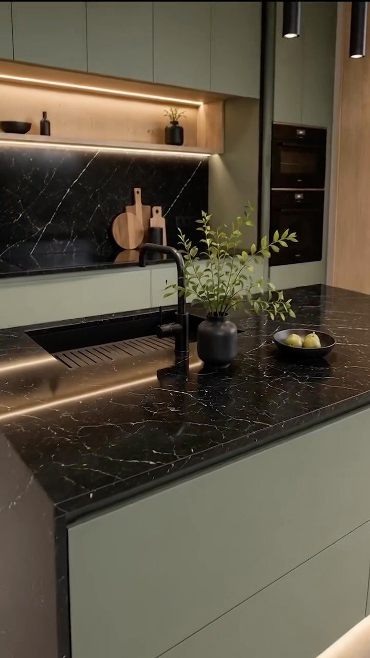 Black marble countertops and backsplash paired with matte sage green kitchen cabinets and warm lighting.