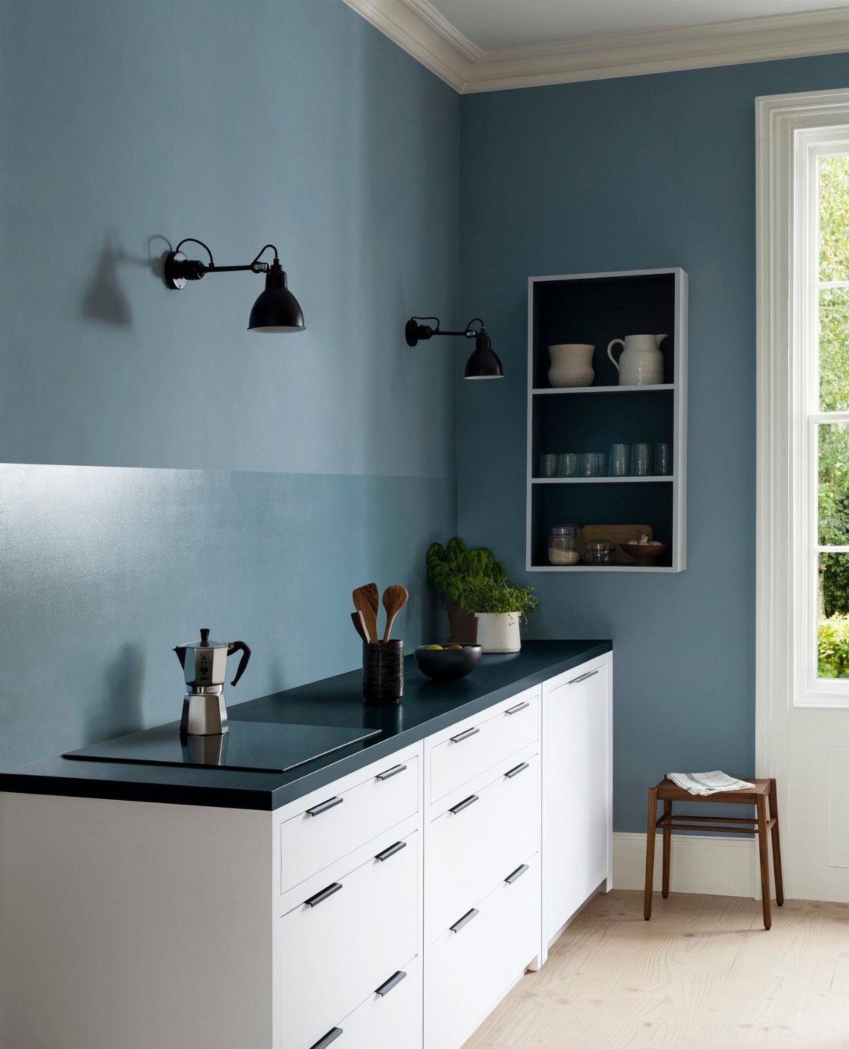 Blue kitchen walls paired with white cabinets and a black countertop under black sconce lights.