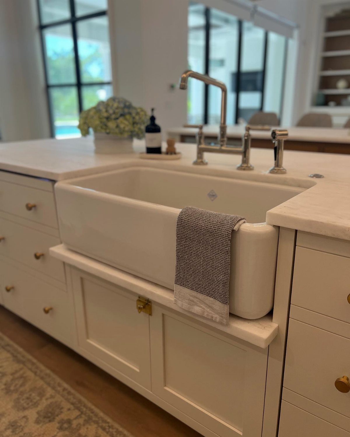A white farmhouse apron-front sink installed in a marble kitchen island with a silver faucet.