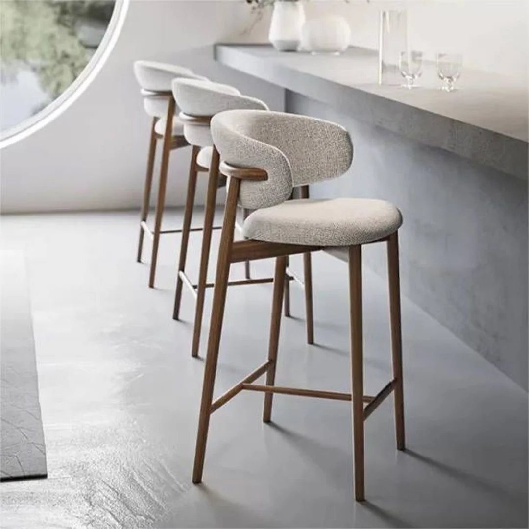Three modern upholstered bar stools with wooden legs lined up along a grey kitchen island.