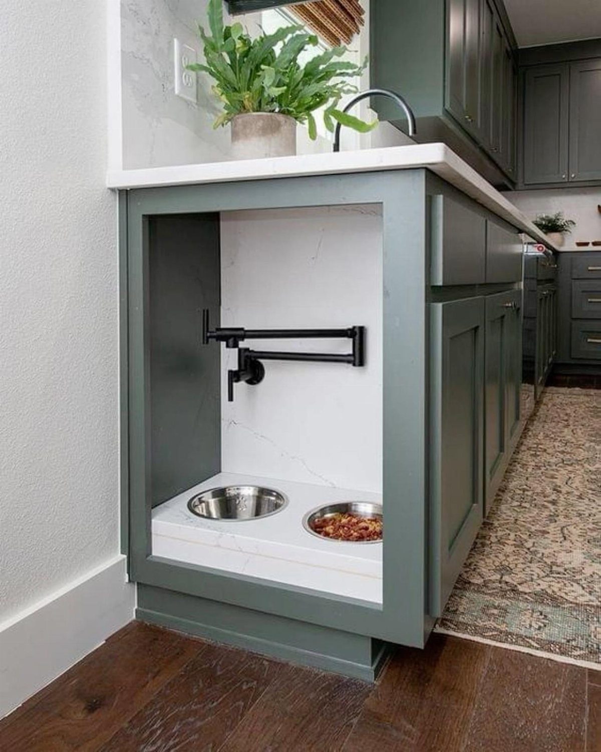 Built-in pet feeding station with stainless steel bowls and a water dispenser in a green kitchen cabinet.