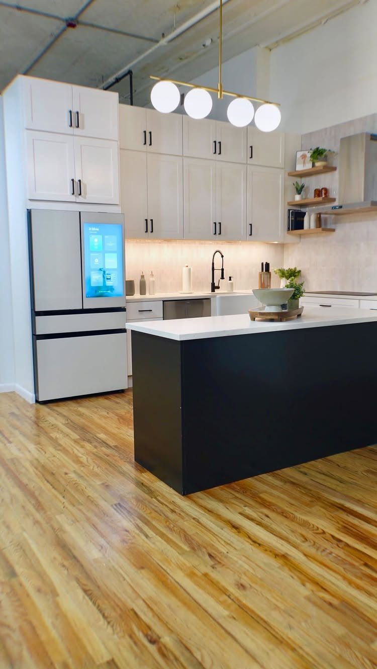 Modern kitchen with white cabinetry, a black island, and a smart refrigerator with a digital screen.