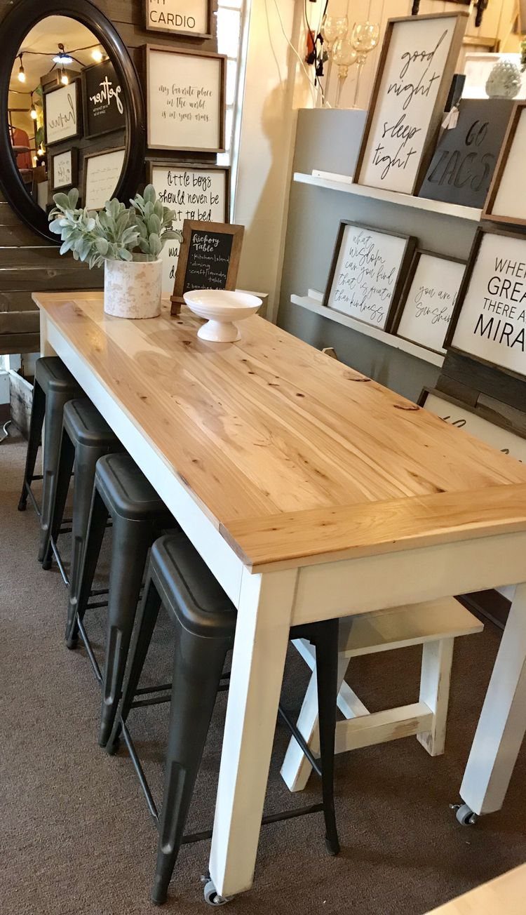 A long wooden dining table with white legs and small caster wheels on the bottom.