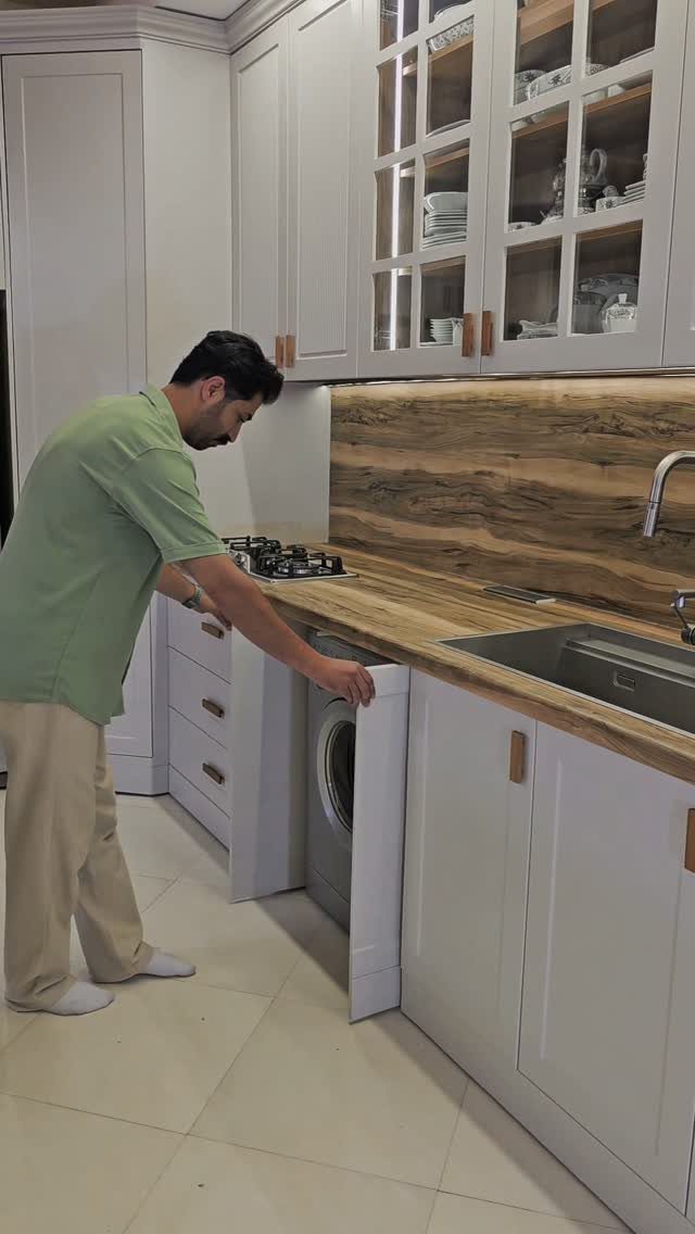 Man opening a white kitchen cabinet to reveal an integrated washing machine underneath.
