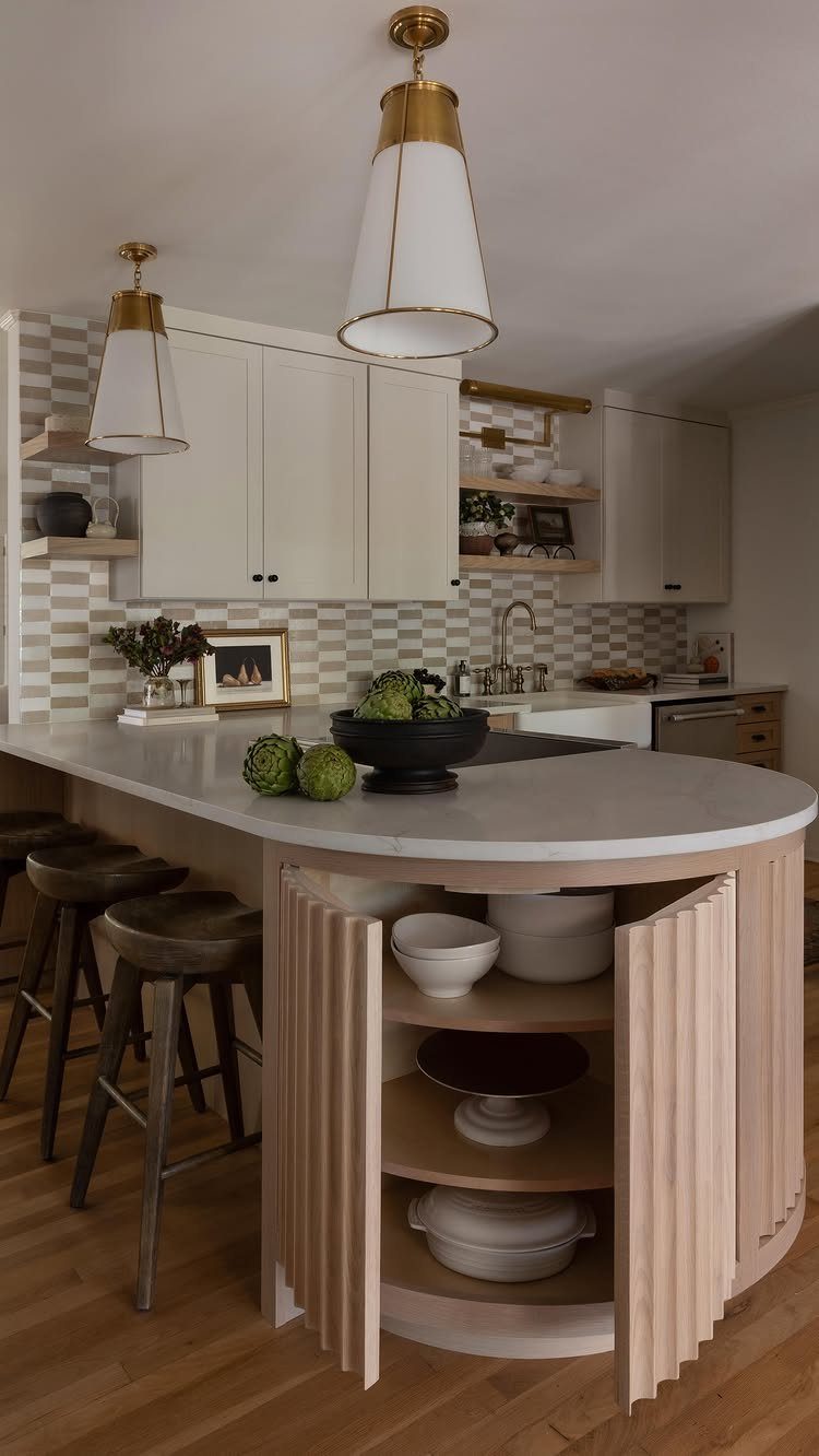 A curved white marble peninsula island with light wood fluted cabinetry and dark wooden bar stools.