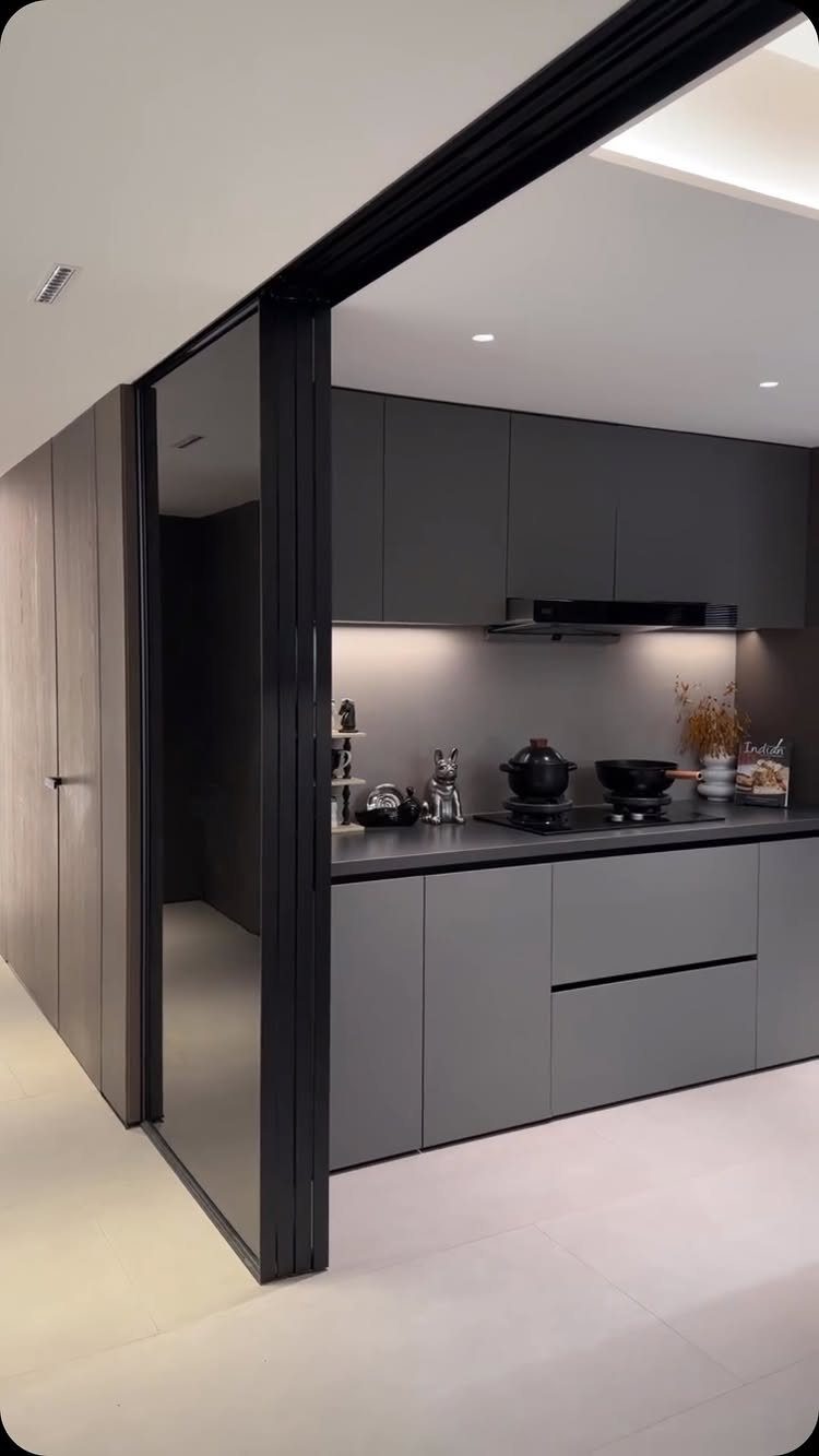 A modern dark grey kitchen viewed through a large black sliding door frame.