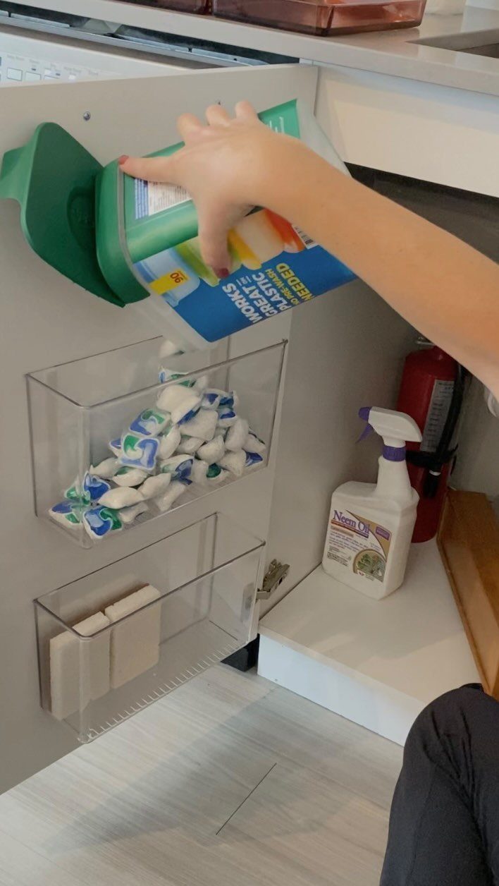 13 Kitchen Organization Ideas for Small Spaces That Free Up Real Room 8 A hand reaches for plastic wrap stored in a clear organizer mounted inside a white cabinet door.