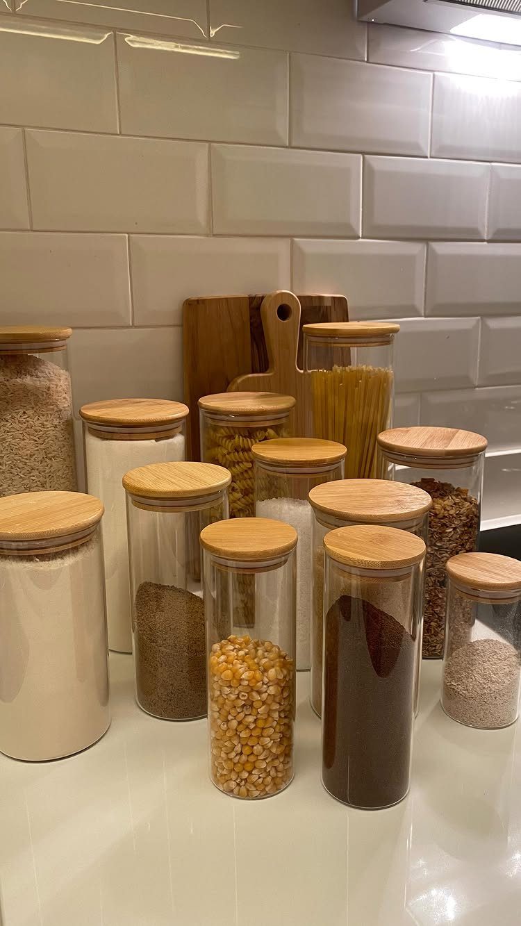 13 Kitchen Organization Ideas for Small Spaces That Free Up Real Room 7 Clear glass canisters with wooden lids containing various grains and pasta on a white counter.