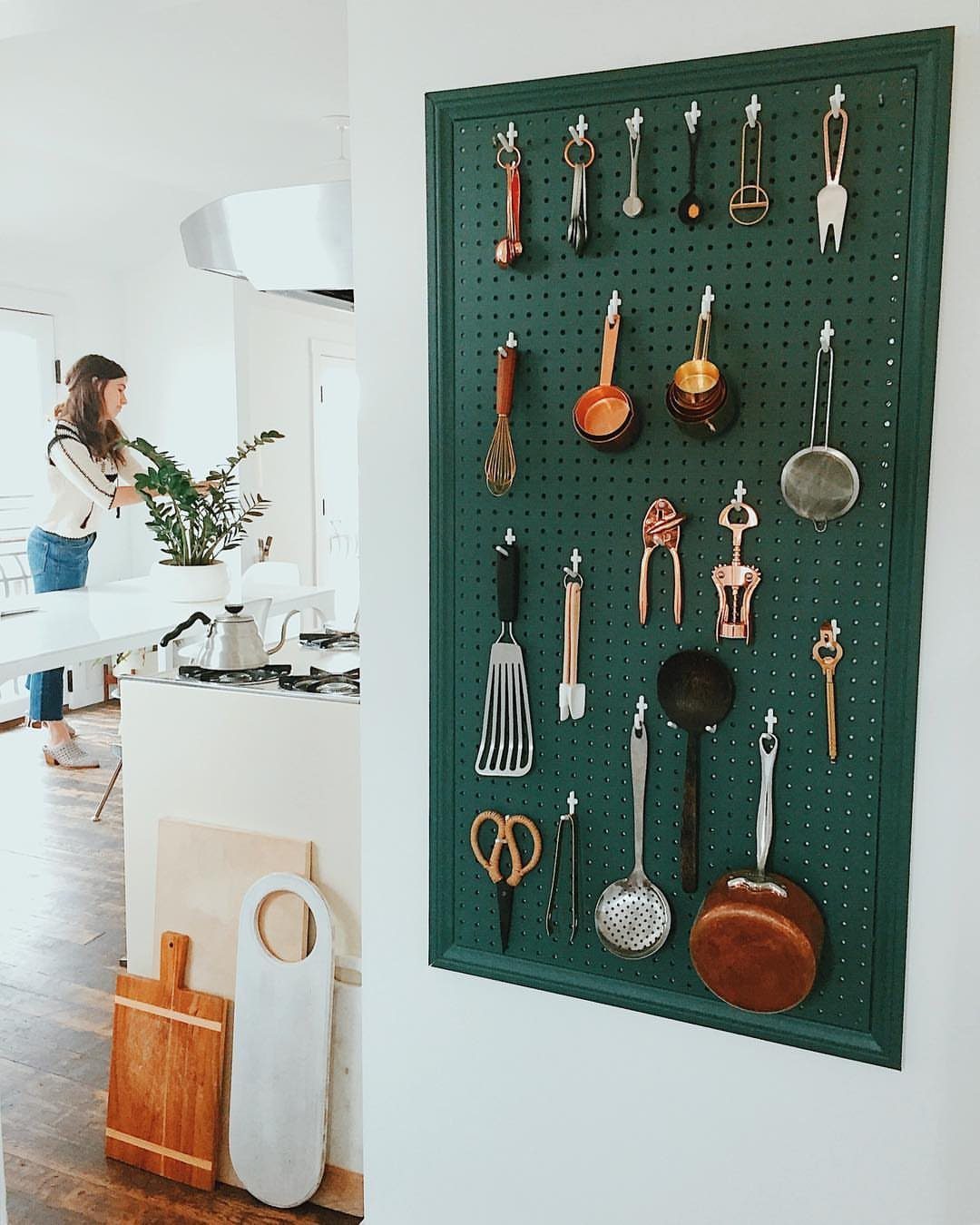 13 Kitchen Organization Ideas for Small Spaces That Free Up Real Room 13 Green pegboard mounted on a white wall holding various metal and wooden kitchen utensils.