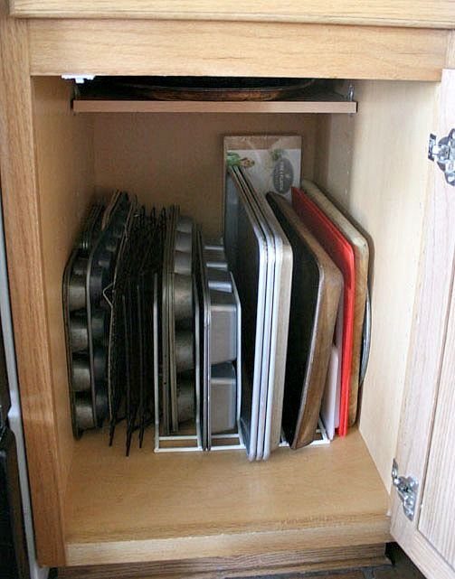 7 Kitchen Storage Tray Ideas for Cabinets and Drawers 4 Baking pans and trays organized vertically inside a wooden kitchen cabinet using white wire racks.