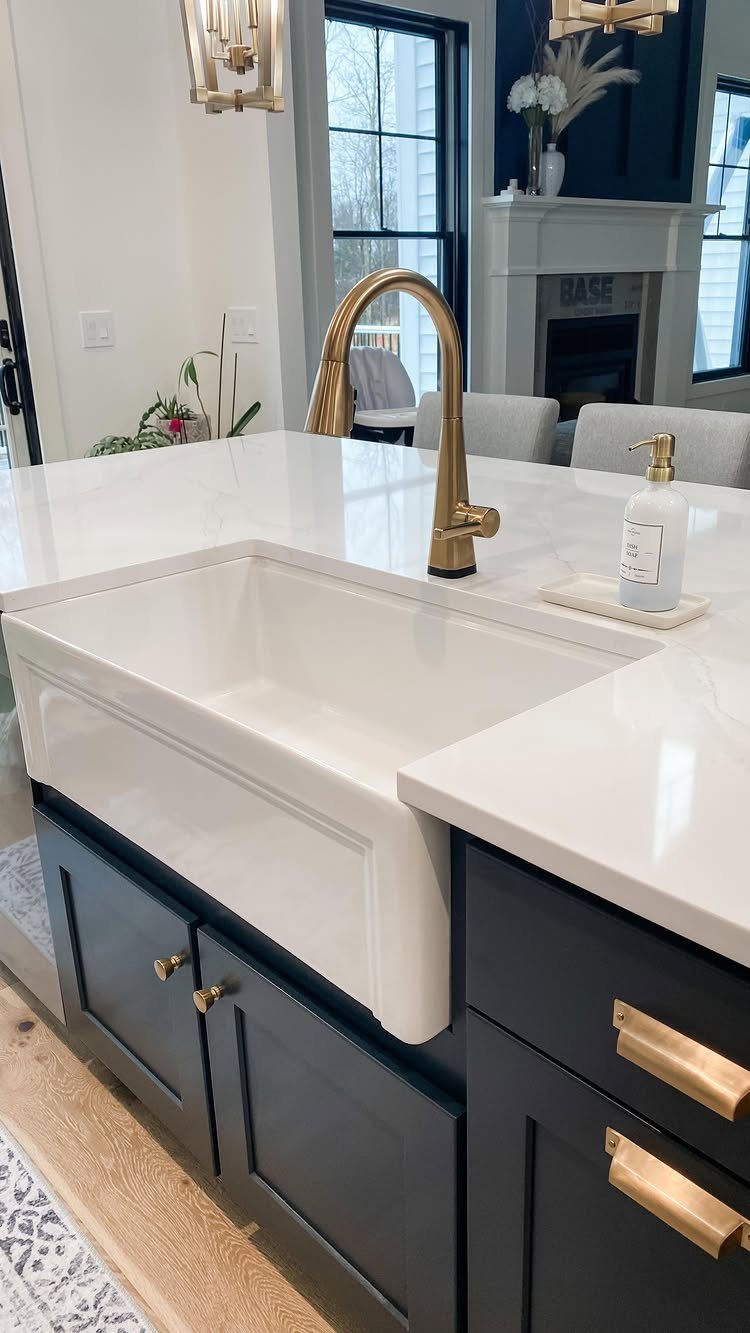 12 Latest Kitchen Sink Design Ideas for 2026 2 A white farmhouse sink integrated into a marble countertop on a dark blue kitchen island.