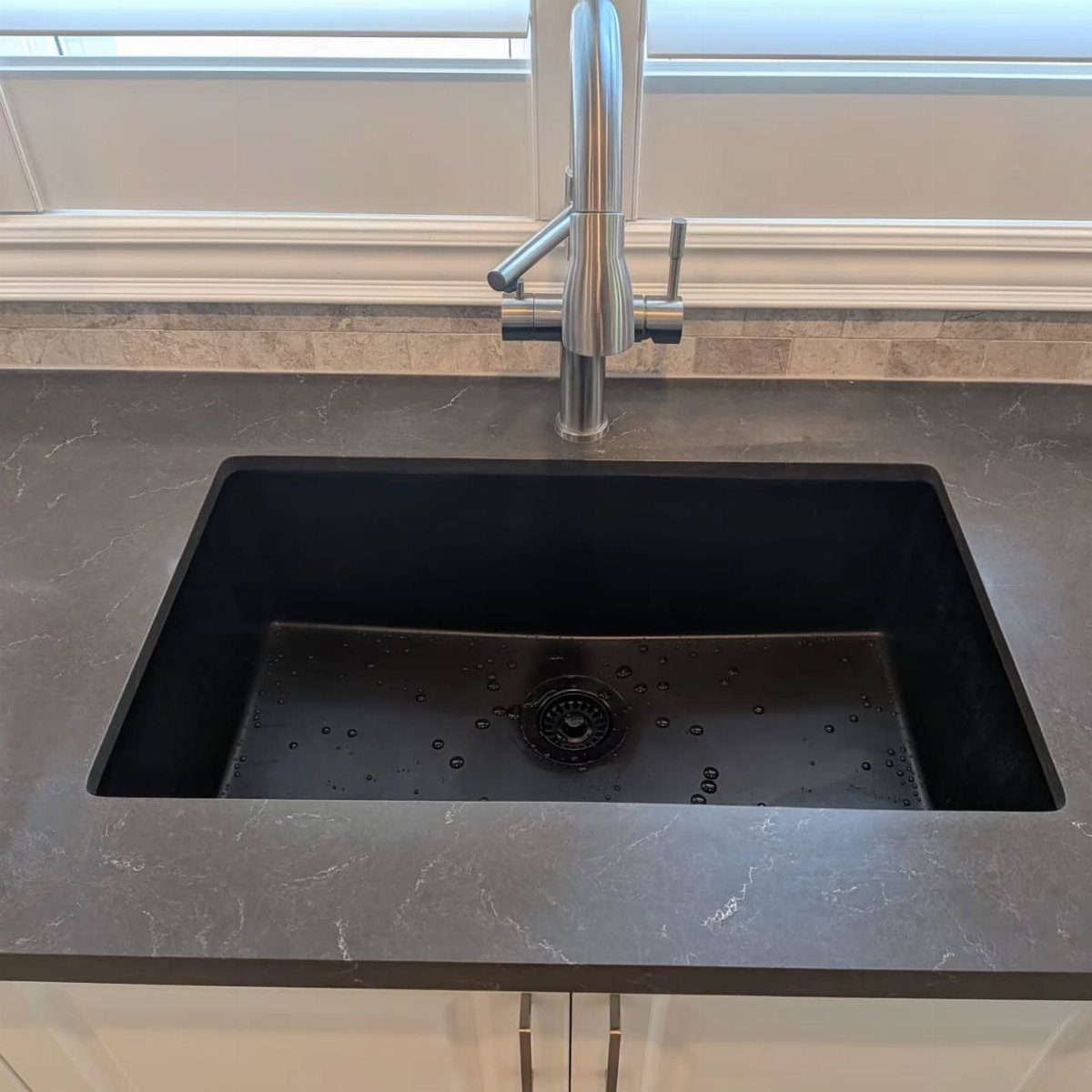 12 Latest Kitchen Sink Design Ideas for 2026 5 A black single-bowl kitchen sink set into a dark grey countertop with a silver faucet.