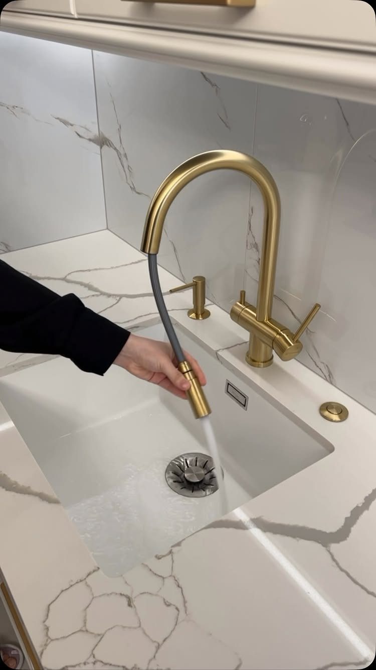 12 Latest Kitchen Sink Design Ideas for 2026 1 A gold faucet running water into a white undermount sink set in marble countertops.