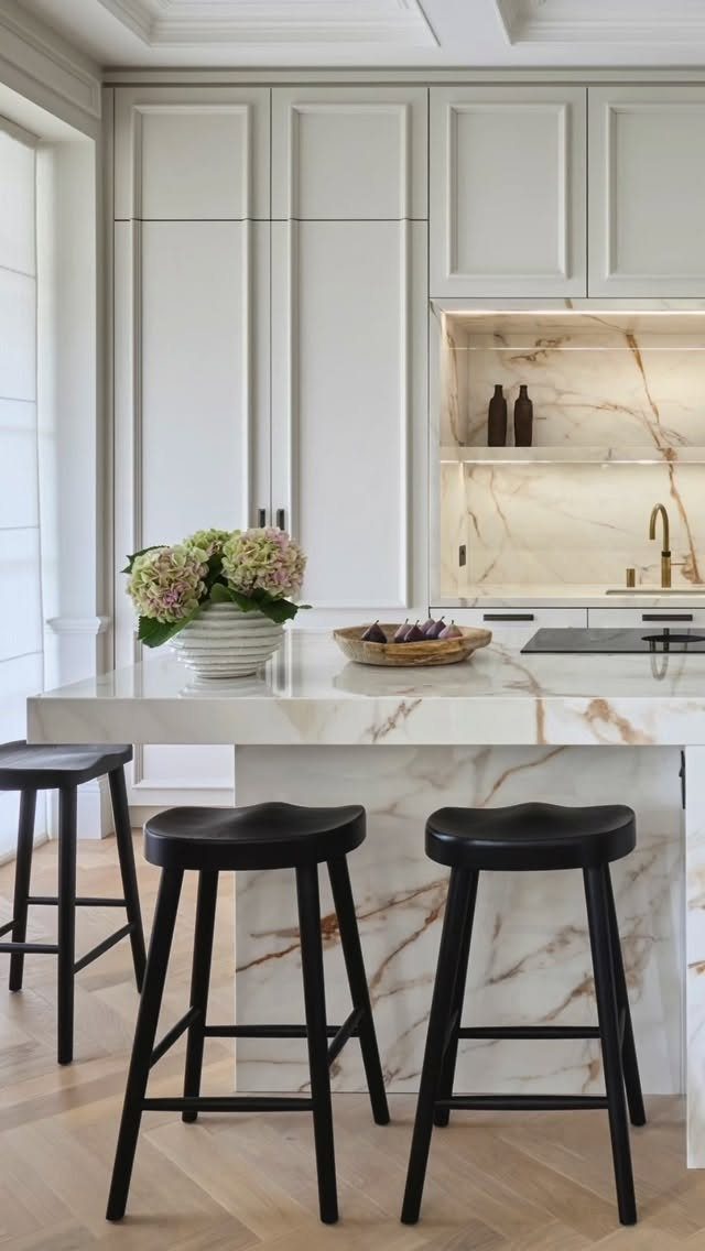 Marble kitchen island with three black stools in a modern white kitchen setting.