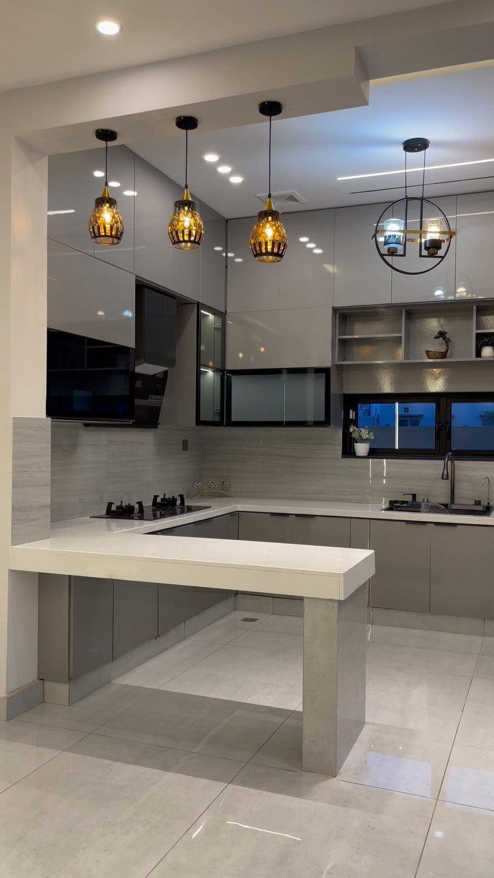 Modern grey modular kitchen with white countertops and amber pendant lights over a breakfast bar.