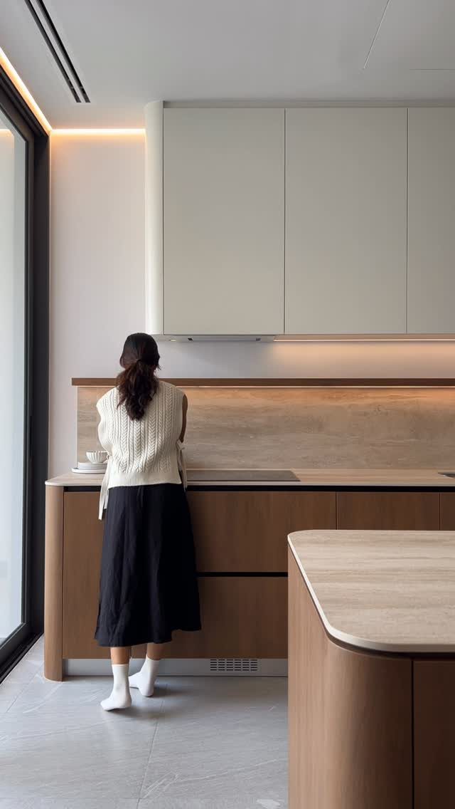A woman standing in a modern kitchen with white upper cabinets and wood base cabinets.