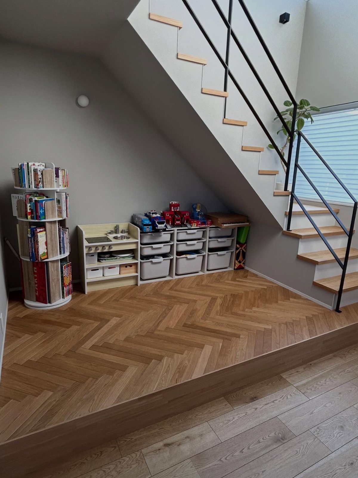 Children's toys and books organized in storage bins and a rotating shelf under a staircase.