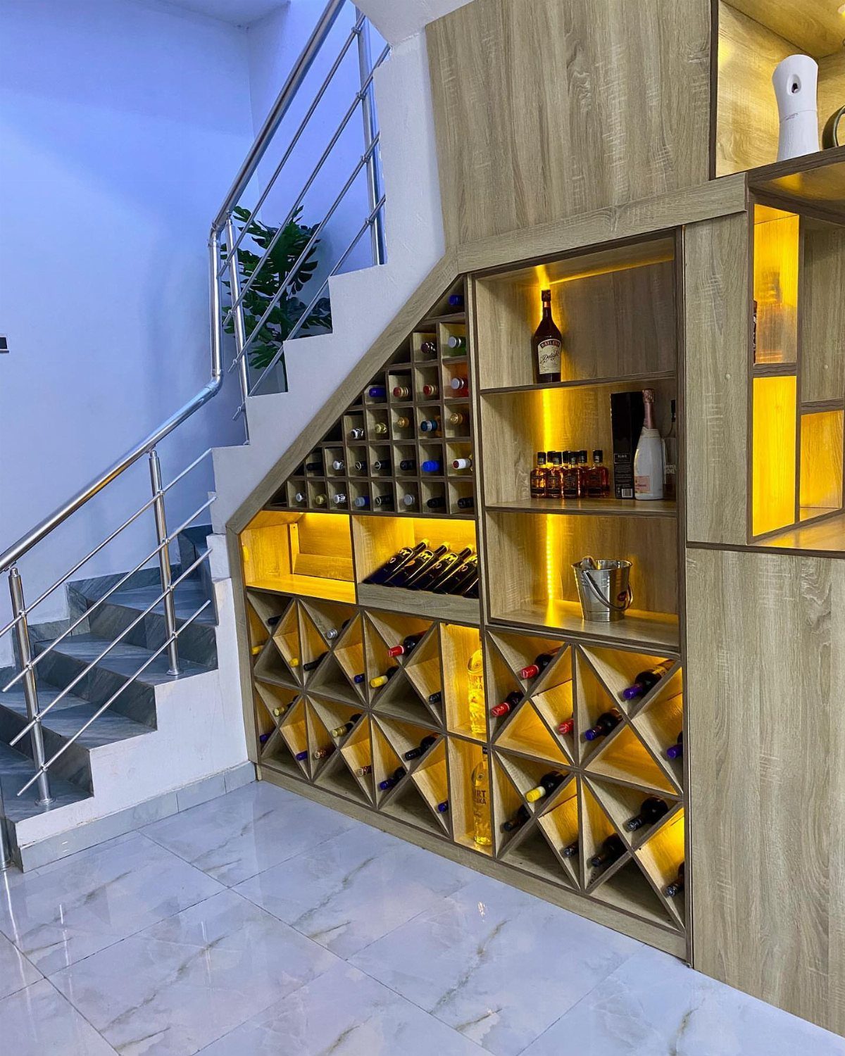 Built-in wooden wine rack and liquor storage unit located underneath a modern staircase.